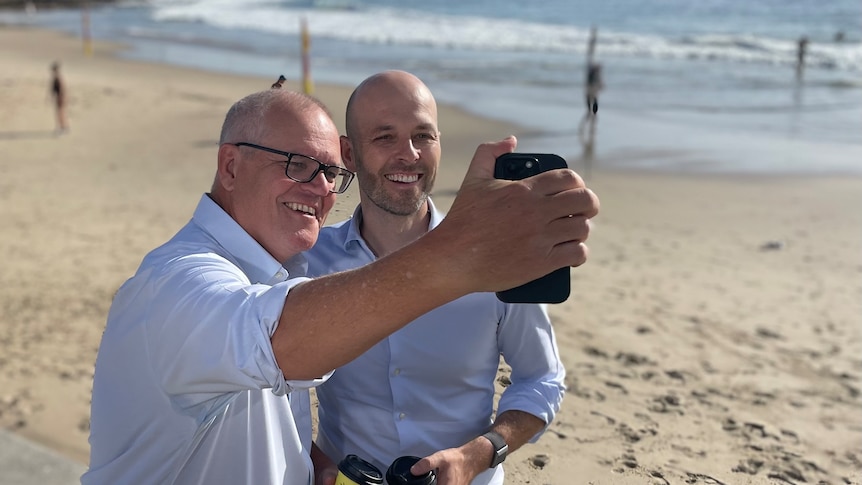 Two men in blue shirts taking photographs on a beach