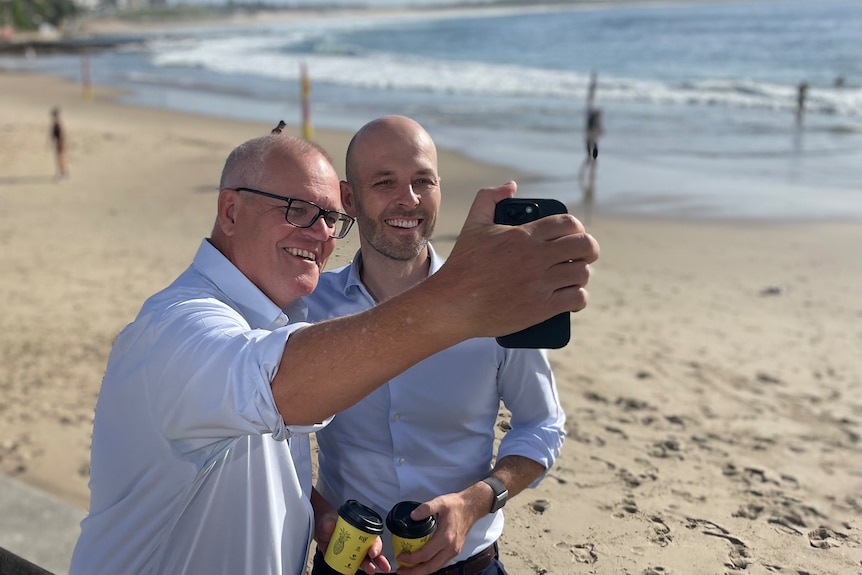 Two men in blue shirts taking photographs on a beach