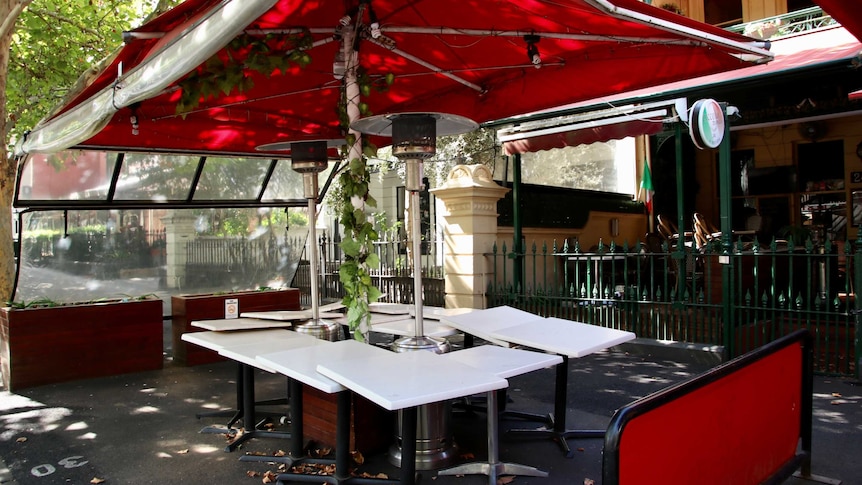 A group of restaurant tables clustered under an umbrella outside.