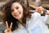 A smiling Aiia Maasarwe holds the two-fingered peace sign up with both hands.