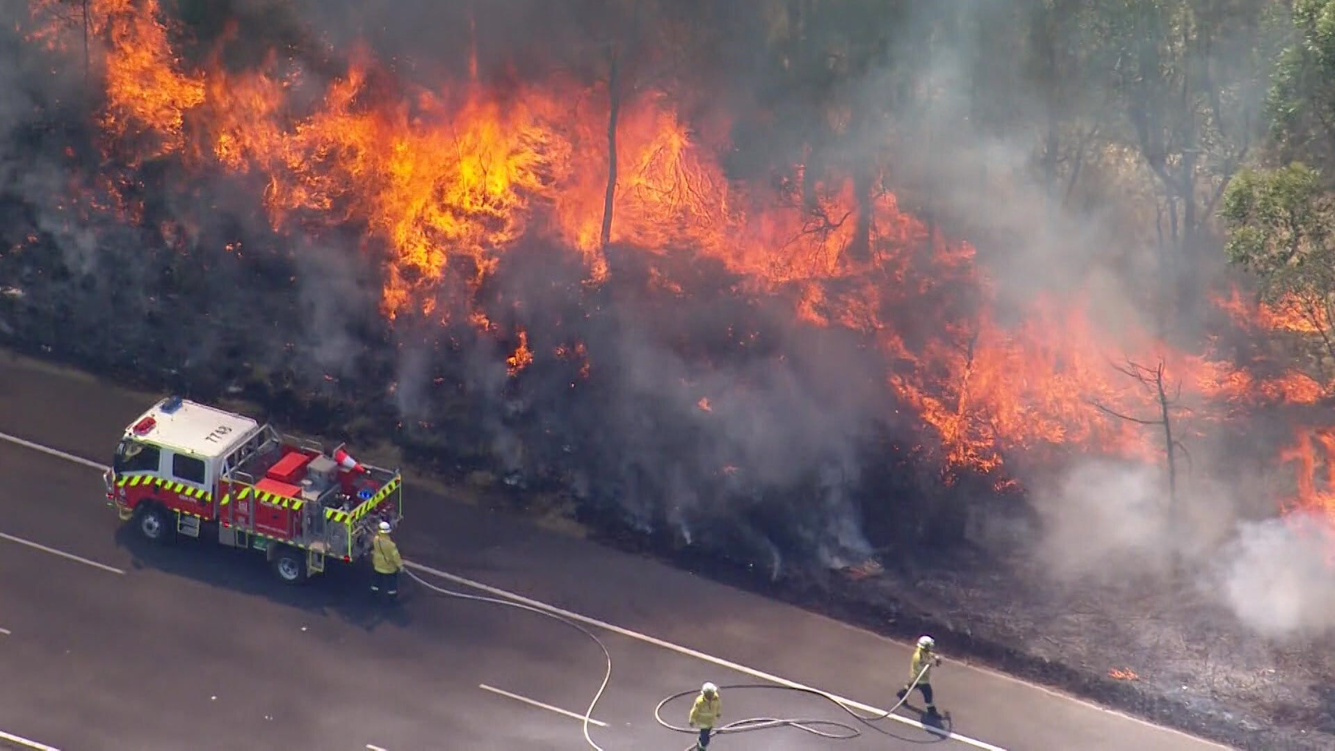 Firefighters battling a grassfire at the side of a road