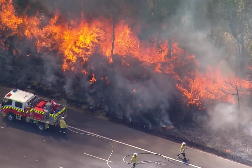Firefighters battling a grassfire at the side of a road