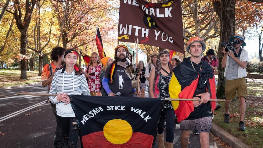 An aboriginal man flanked by aboriginal youth walking behind an aboriginal flag in Canberra