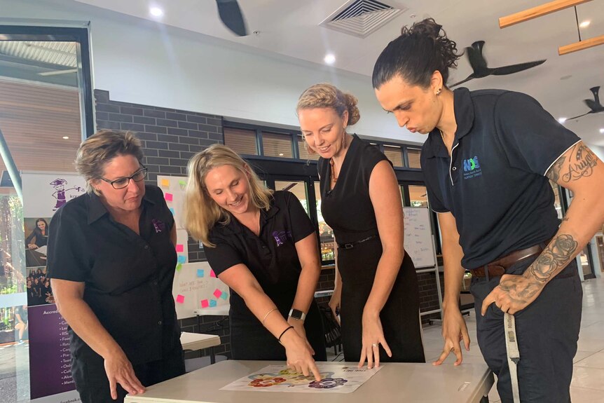 Susan Burns stands with colleagues who are looking at a sheet of paper on a desk.