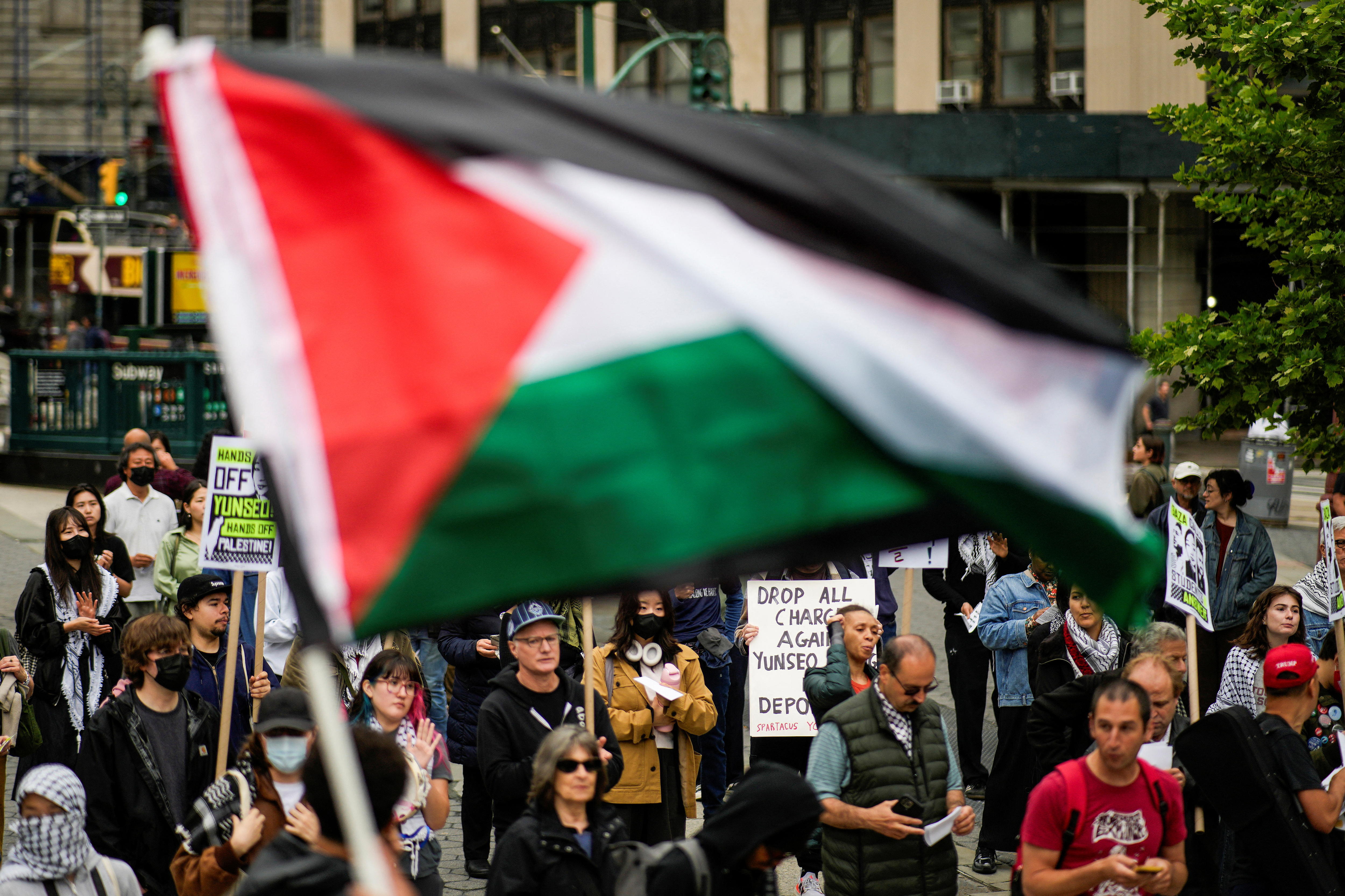 A crowd of people protests with a Palestinian flag in the foreground