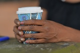 A woman's hands hold a coffee cup which has bright patterns on it. A lighter is also on the table.