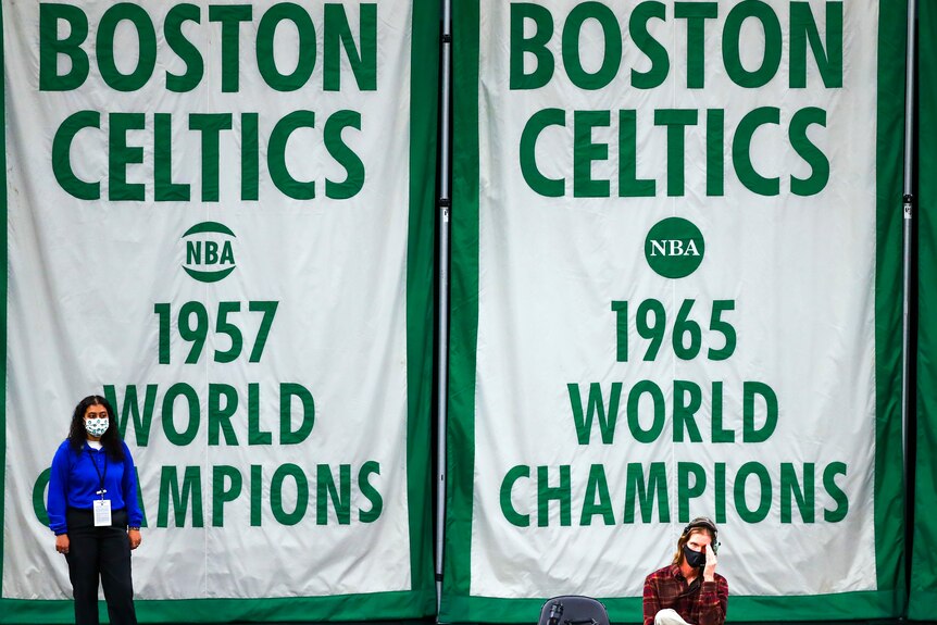 the Boston Celtics' 1857 and 1965 championship banners hang behind two people in face masks.