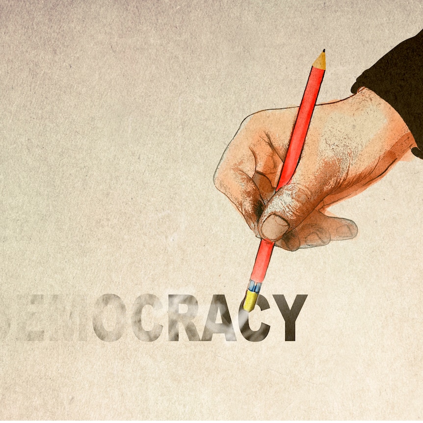 A hand holding a pencil to erase the word democracy