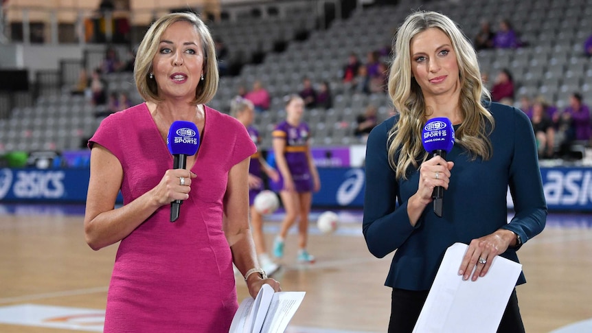 Two netball commentators stand holding microphones at courtside before a Super Netball match.
