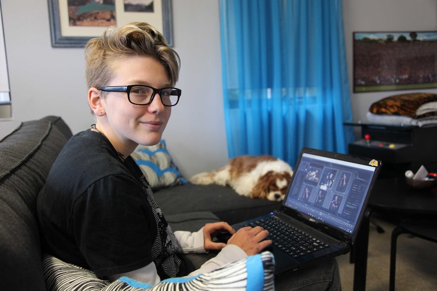 Leon, 16, sits at his laptop on a couch with a dog asleep next to him.