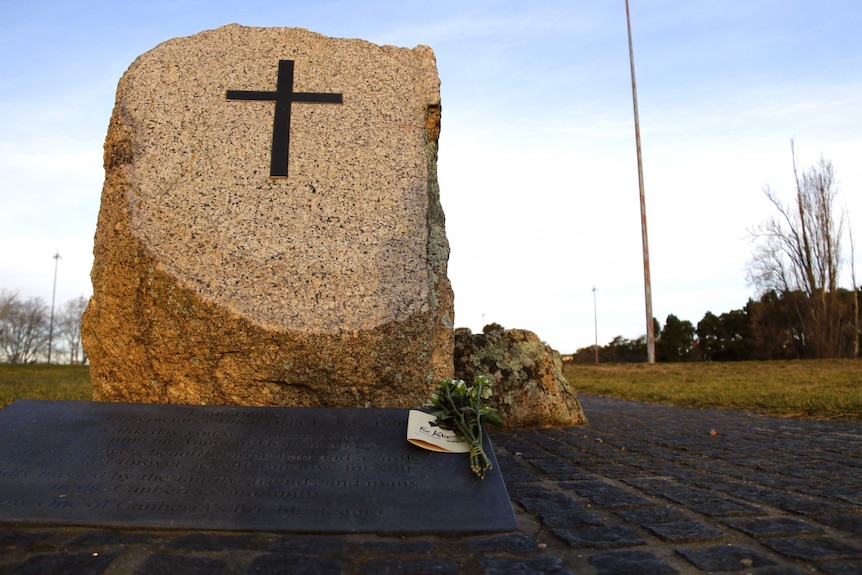 A stone memorial with flowers placed at the base along with a card which reads "for Katie".