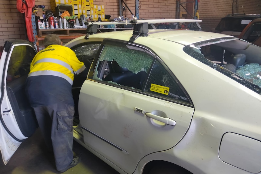 A man in high-vis works on a damaged car in a garage.