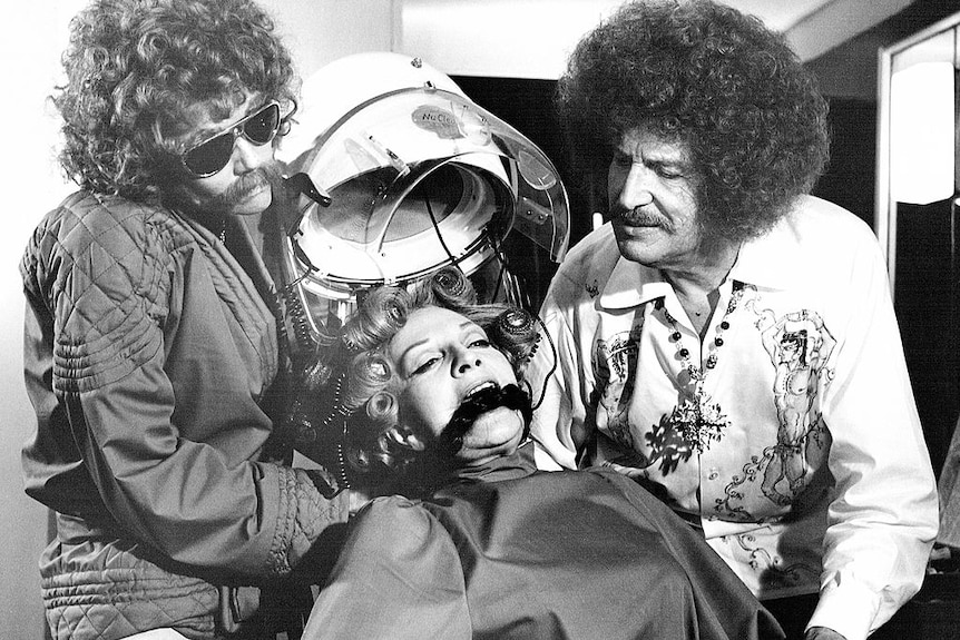 Black and white picture of three actors, one in a hairdressing chair 