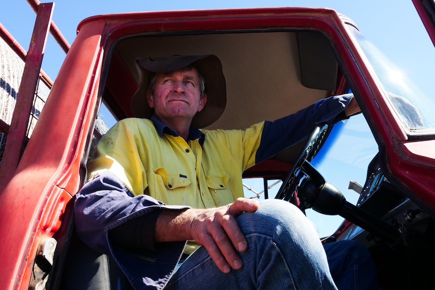A man sits in the cabin of an old truck. He is wearing a hat.