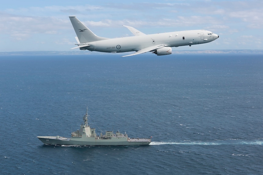A RAAF Poseidon jet flies above the destroyer HMAS Hobart.