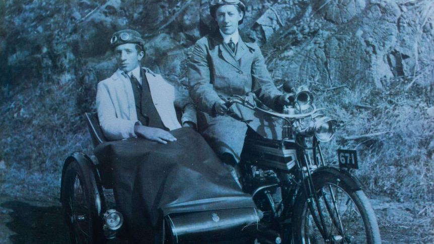 Aged monochrome photo of a man astride a motorcycle and another in a sidecar