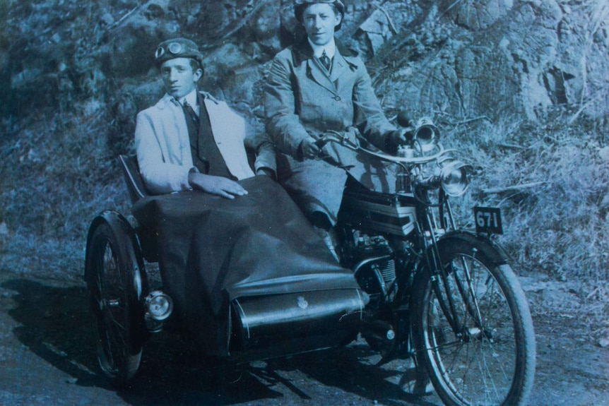 Aged monochrome photo of a man astride a motorcycle and another in a sidecar