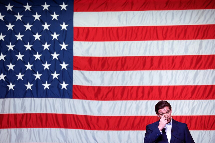 Ron DeSantis touches his face in front of an American flag