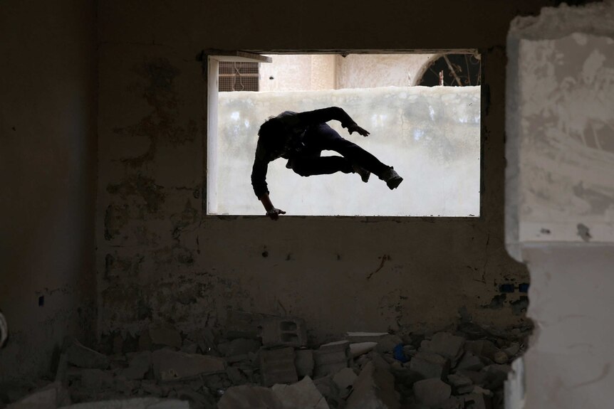 The silhouette of Syrian man can be seen as he jumps through the window of a damaged building in the Syrian city of Inkhil.