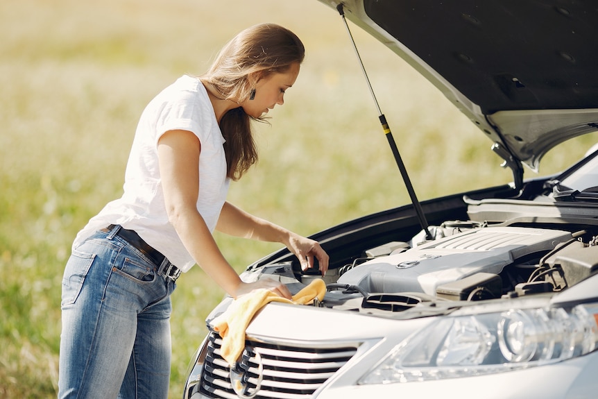 A woman checks her car's engine.