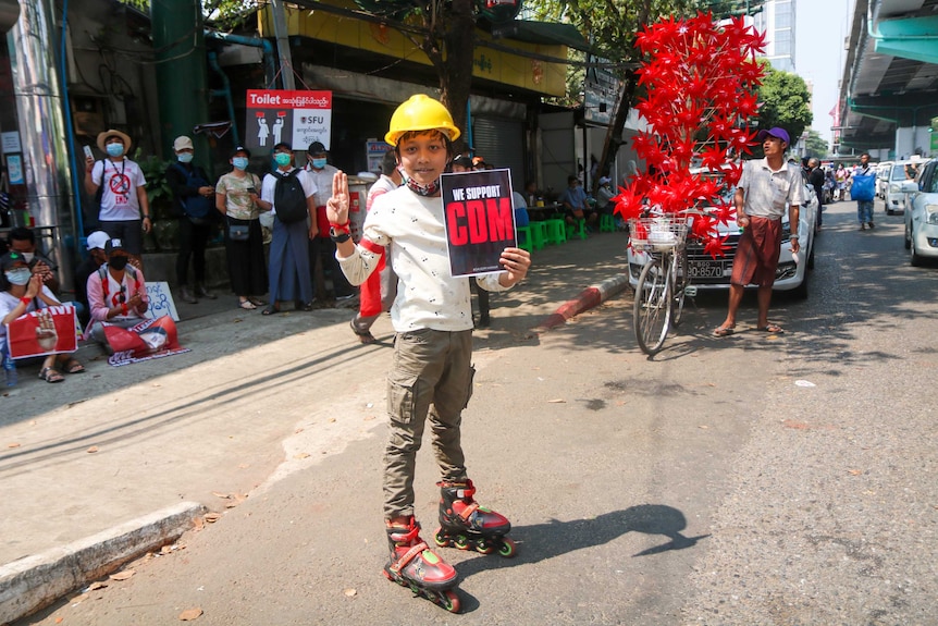 A boy wearing a yellow helmet holds up three fingers and holds a sign saying "we support CDM".