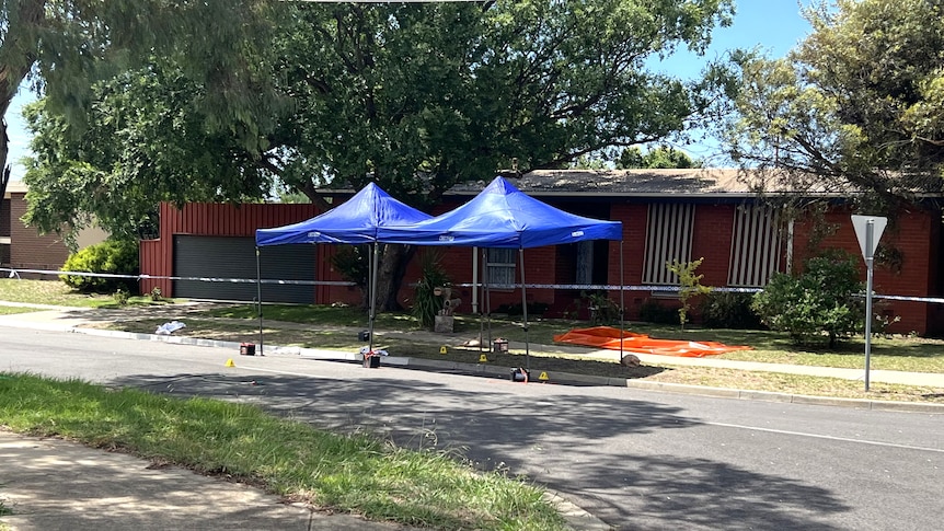 Police tape around a house with several tents also set up