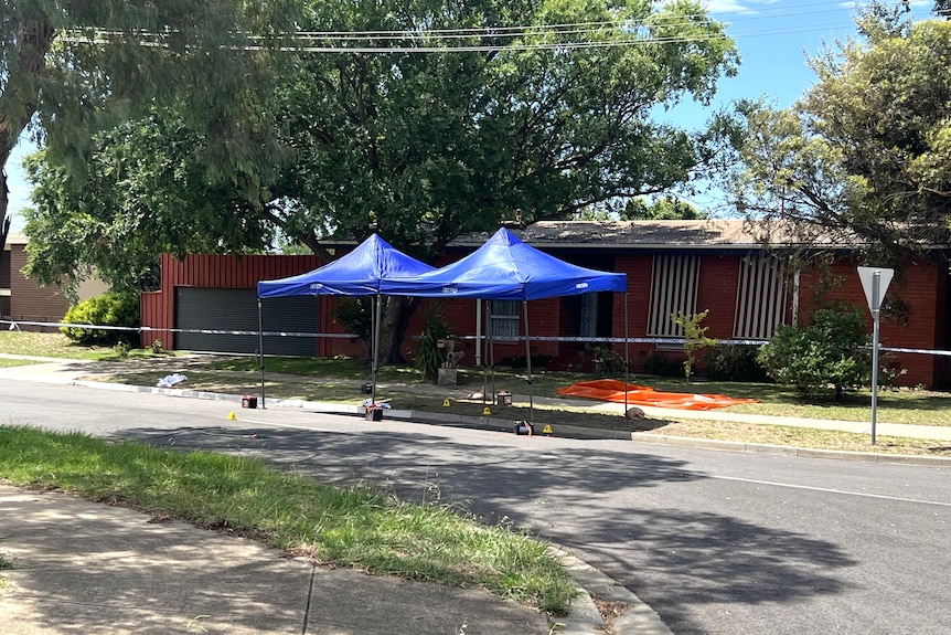 Police tape around a house with several tents also set up