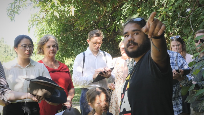 Aboriginal man pointing and talking to people gathered around him.