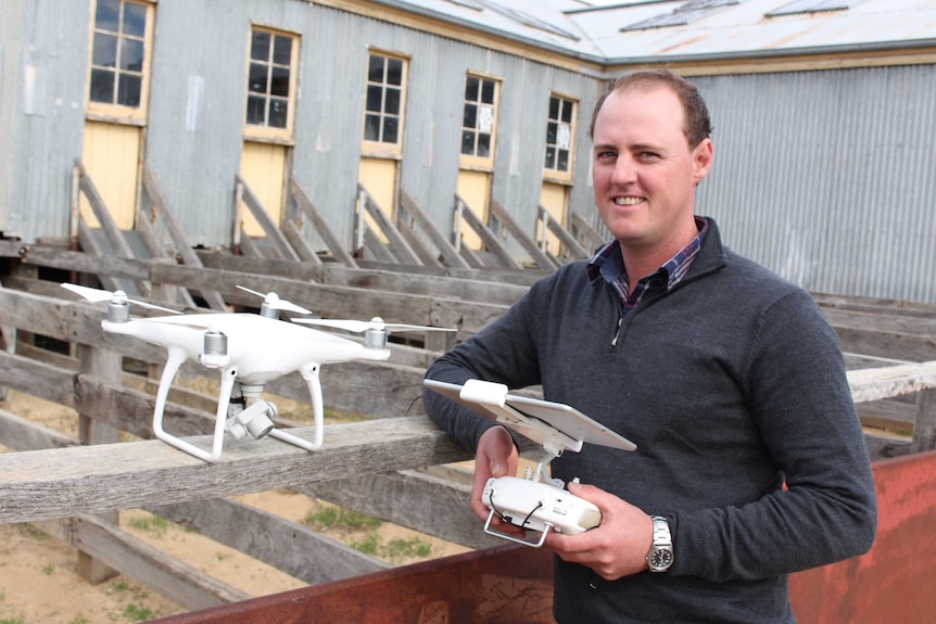 A man standing in stockyards, with a white drone perched on a rail.