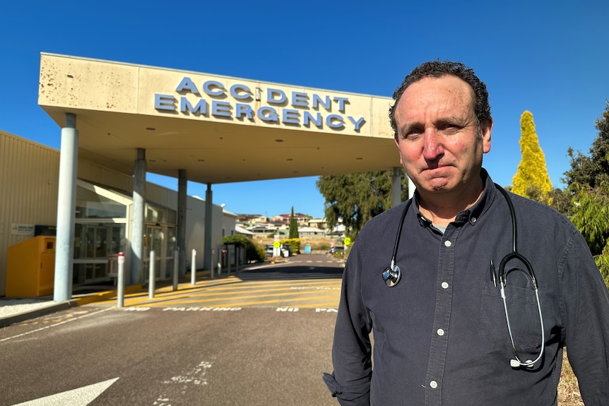 A man stands in front of an emergency department entrance.