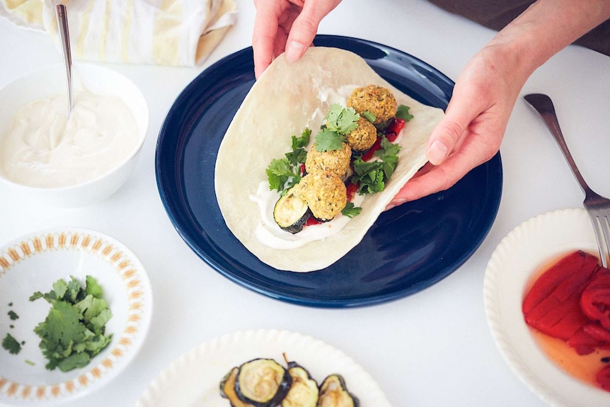 Four falafel balls sit atop a flatbread with yoghurt sauce, grilled capsicums, roasted zucchini and coriander, a family dinner.