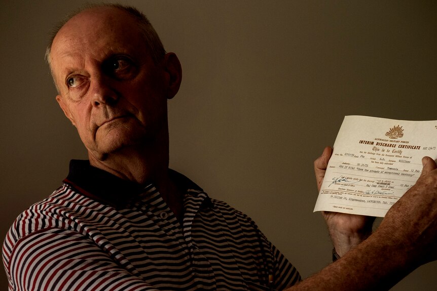 A man in his 70s holds a small discharge certificate from the Australian Defense Force.