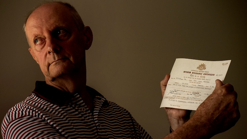 A man in his 70s holds a small discharge certificate from the Australian Defense Force.