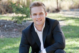 A young man in a business suit kneels on grass