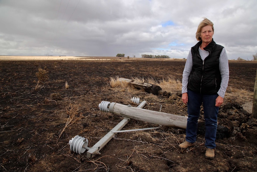 Betty Kenna standing next to a power pole on the ground.