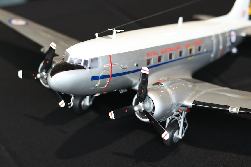 A close-up photo of the nose and propeller on a silver and white model aeroplane on a table.