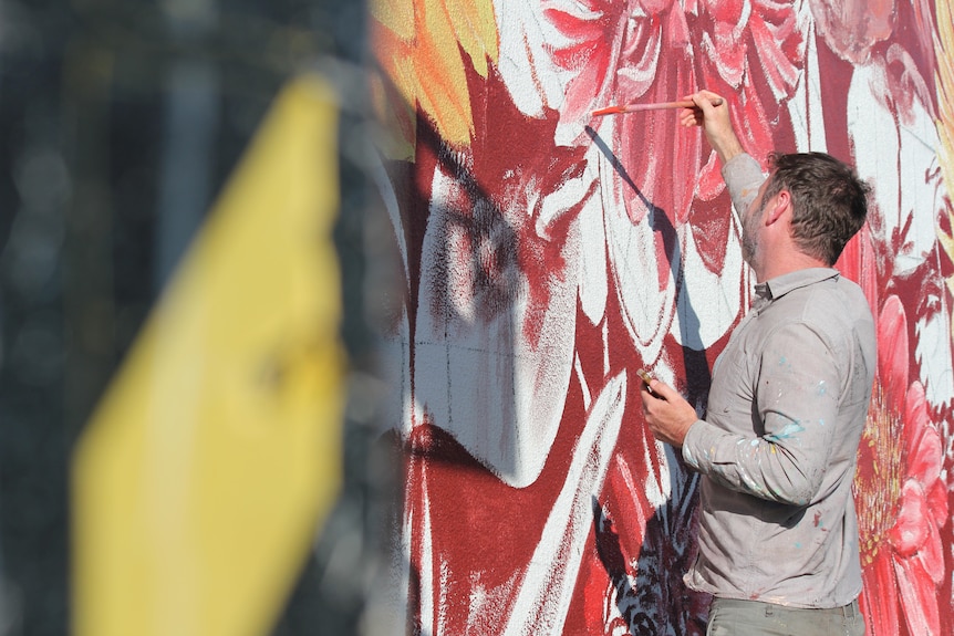 A painter puts color onto a mural of a sunflower