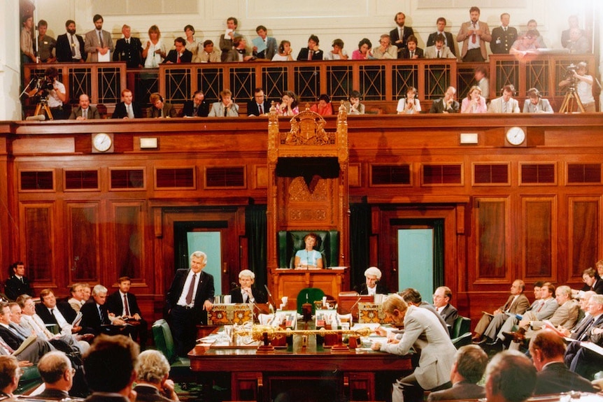 Shot of journalists and TV crews in gallery watching Hawke on floor of parliament speaking.