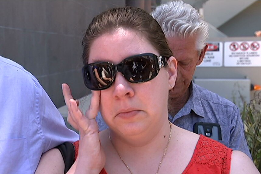 Close up of Melanie Michell wearing sunglasses and wiping a tear from her eye.