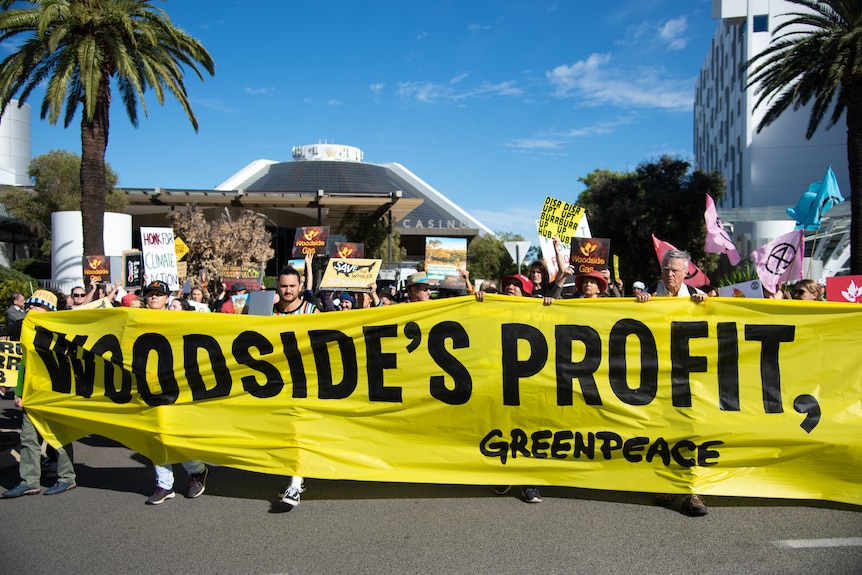 A group of protesters holding a large yellow sign saying "Woodside's profit".