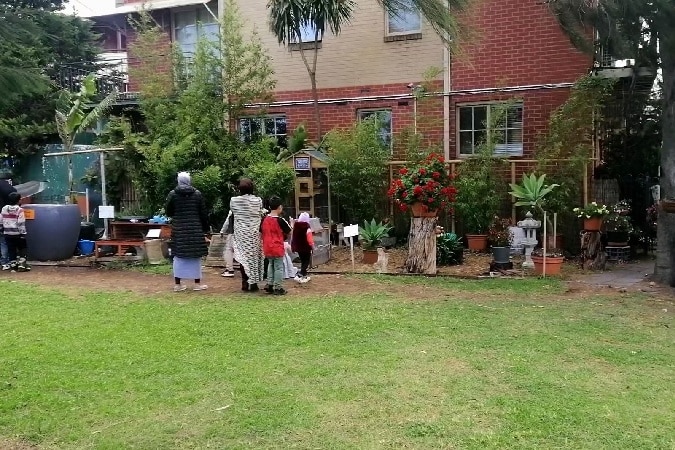 A group of people are looking at the flowers and animals in the park outside an apartment building.