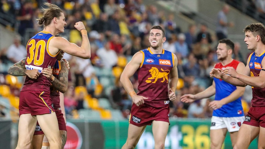 An AFL player punches the air with his fist after scoring a goal, as his teammates look on.