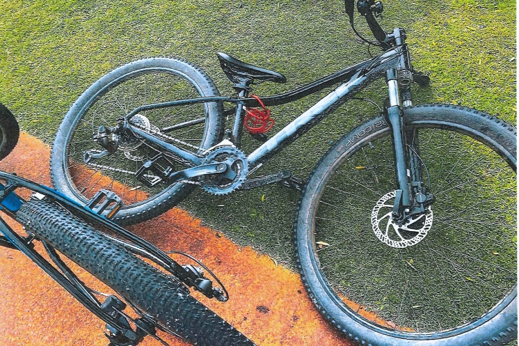 A bike lying on the ground with two other bikes in the background, and police tape to the left. 