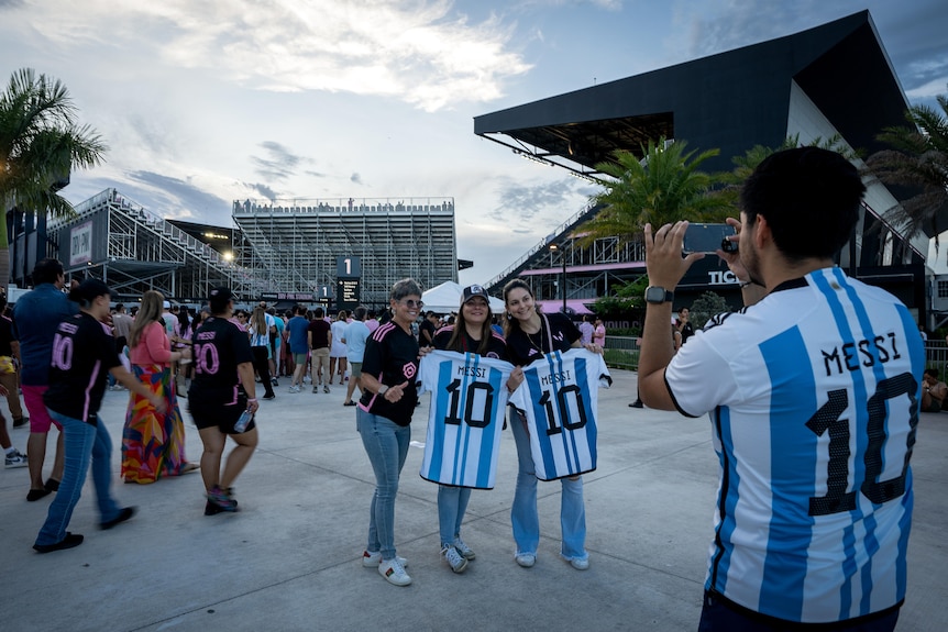 Messi fans pose with his Argentina jersey, white and blue stripes with 10 on the back, as another person takes their picture