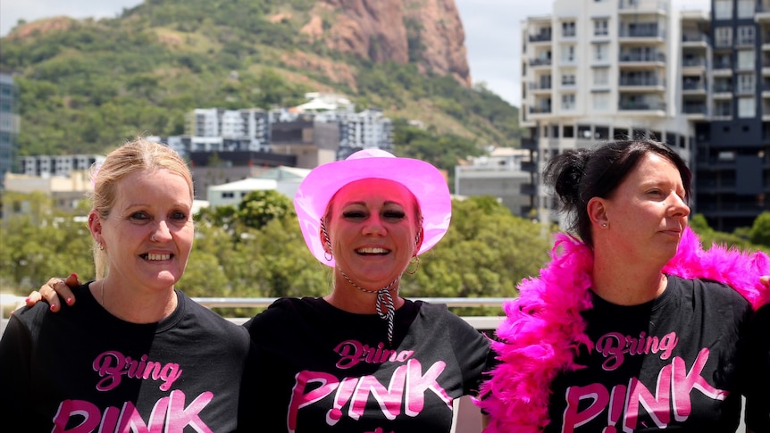 Three women in front of Castle Hill, wearing Bring Pink to Townsville T-shirts.