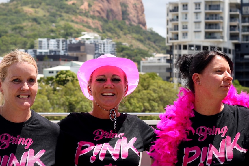 Three women in front of Castle Hill, wearing Bring Pink to Townsville T-shirts.