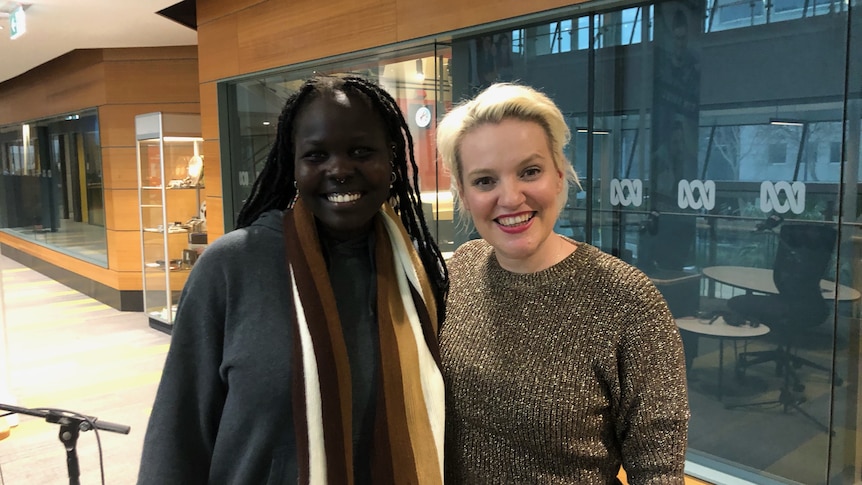 two women standing next to each other outside a glass-walled radio studio