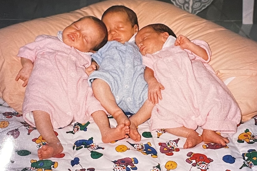 Baby triplets sleeping huddled together on a v-shaped pillow in the 1990s