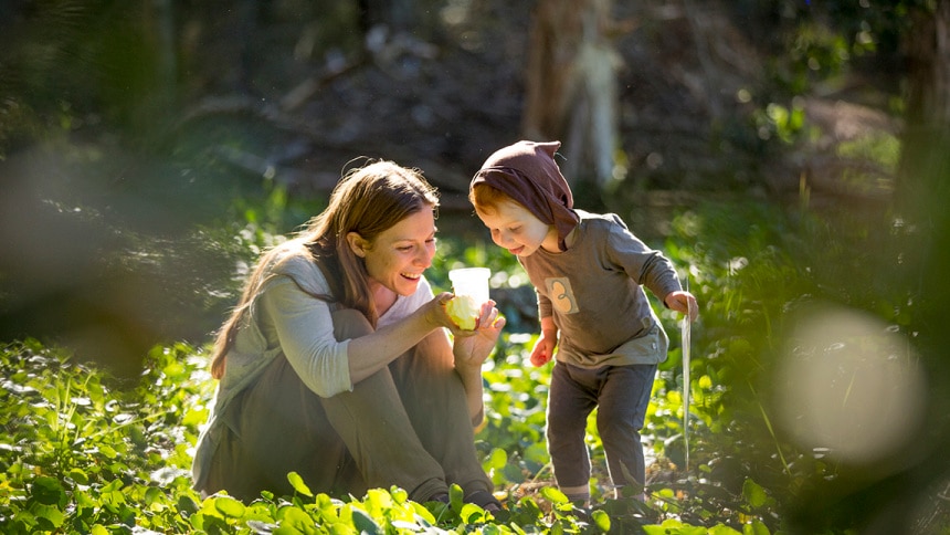 a mother and child look in wonderment at a bug in a grassy field