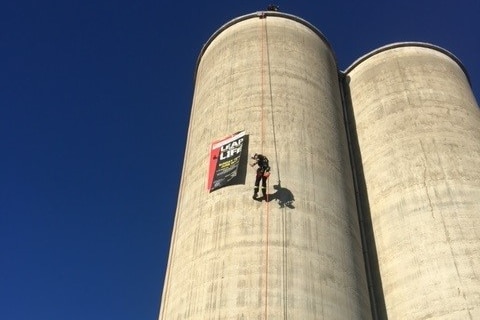 A person abseils down a grey silo